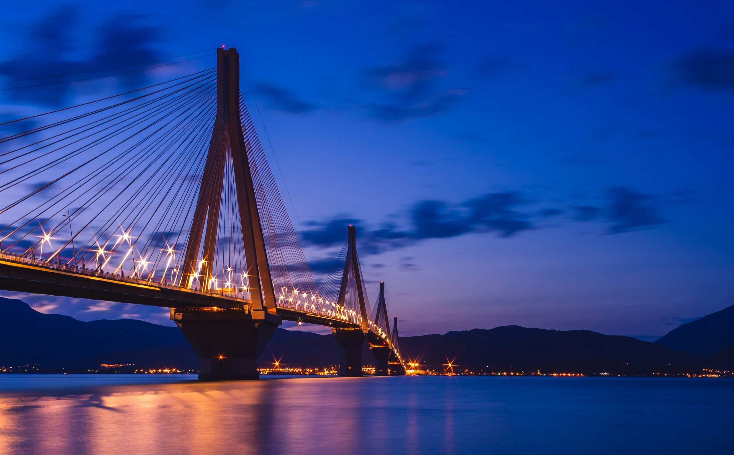The Rio–Antirrio bridge lit up at dusk over the Gulf of Patras